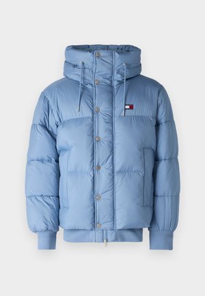 Lys blå pufferjakke med hette, trykknapper, sidelommer og ribbestrikkede mansjetter. Har en logo-patch på brystet. Glatt tekstur.