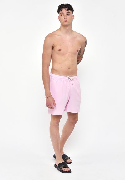 Costumi da bagno rosa chiaro con vita elastica e cordoncino, abbinati a sandali neri a infradito. Tessuto liscio, design fino al ginocchio.