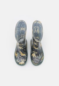 Bottes de pluie pour enfants avec des semelles vertes, ornées de motifs jaunes d'animaux et de feuilles sur un fond sombre, vues du dessus.