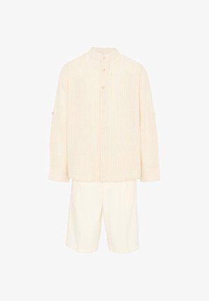 Camicia crema a maniche lunghe con righe verticali e bottoni dorati abbinata a pantaloncini bianchi al ginocchio su sfondo bianco.