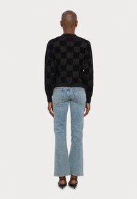 Pull en maille noir avec un motif à carreaux et un ourlet côtelé, associé à un jean flare bleu clair et des talons noirs à lanières.