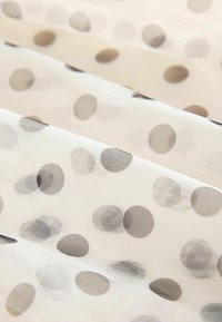 Tissu transparent avec un fond blanc comportant des pois noirs éparpillés de différentes tailles ; texture lisse avec un design léger.