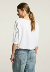 Biały, krótki top z luźnym krojem, zestawiony z jasnoniebieskimi dżinsami z wysokim stanem, które mają tylne kieszenie i lekko wypłowiały wygląd.