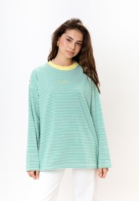 Langarmshirt met groen en witte strepen, een gele geribde kraag en een relaxte pasvorm. Zacht materiaal met subtiele geborduurde details.