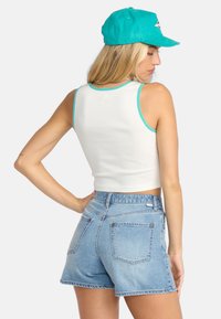 White cropped tank top with turquoise accents paired with light blue denim shorts. The fabric is soft with a slight stretch.
