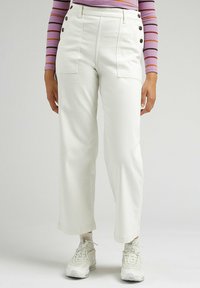 Vita vida byxor med hög midja, med sidofickor och metallknappdetaljer, i kombination med vita sneakers.