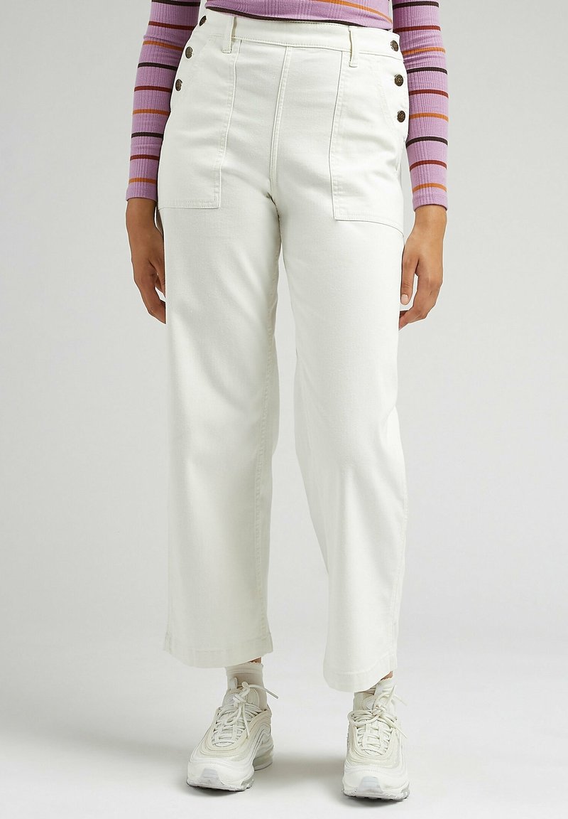 Vita vida byxor med hög midja, med sidofickor och metallknappdetaljer, i kombination med vita sneakers.