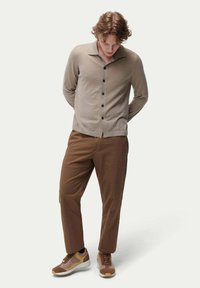 Beige knapplistad cardigan med krage och svarta knappar, matchad med bruna byxor och bruna sneakers med gula detaljer.