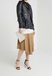 Zwarte leren motorjack, crèmekleurige en bruine jurk met kleurvlakken, lichtgrijze clutch met patroon en zwarte hoge haksandalen met bandjes.