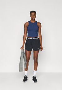 Μπλε αμάνικο τοπ, μαύρες σορτς Nike Pro με λευκή ελαστική μέση, γκρι τζάκετ κρεμασμένο στο ένα χέρι, μαύρα αθλητικά παπούτσια, λευκές κάλτσες.