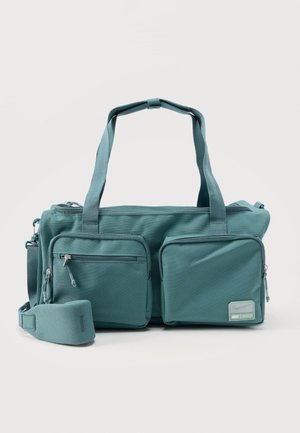 Teal fabric duffel bag with two large front zip pockets, dual carry handles, and detachable padded shoulder strap on white background.