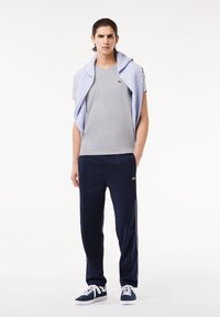 Szary t-shirt z dekoltem w serek, jasno niebieski sweter dzianinowy zarzucony na ramionach, granatowe spodnie dresowe z bocznymi paskami i granatowe sneakersy.
