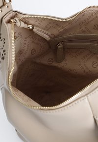 Beige handtas interieur met een gladde leerstructuur, gouden rits en een beige voering met een herhaald logo patroon. Inclusief een ritsvak.
