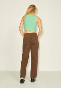 Top corto de color verde menta combinado con unos pantalones de tiro alto marrones. Los pantalones tienen bolsillos traseros y un diseño de pierna recta. Unos zapatos negros completan el conjunto.