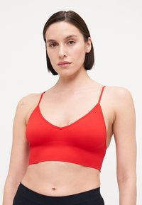 Bralette rouge à côtes avec un décolleté en V et de fines bretelles. Il présente un design ajusté et une longueur courte. Texture lisse sur l'ensemble.