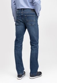 Camisa abotonada de color azul claro con pantalones vaqueros de mezclilla azul oscuro. Los pantalones cuentan con dos bolsillos traseros, detalles de costura y un diseño de pierna recta.