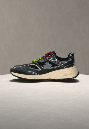 Scarpa da ginnastica nera e beige con lacci rossi e gialli, dettagli in mesh e un motivo a foglia d'acero sul lato, mostrata su una superficie chiara.