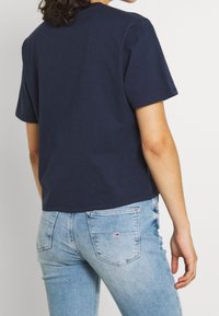 Camiseta de algodón azul marino de corte relajado, con mangas cortas y escote redondeado. Combinada con jeans ajustados de color azul claro con bolsillos traseros.