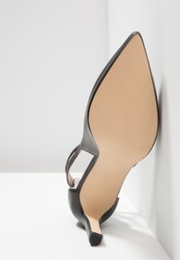 Chaussure à talon noir avec un bout pointu, tige en cuir lisse, design à côté ouvert et un talon aiguille mince ; semelle texturée de couleur claire.