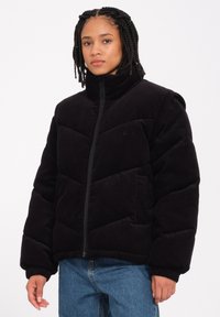 Schwarze Cordjacke mit hohem Kragen, Reißverschluss und gestepptem Design. Verfügt über elastische Bündchen und seitliche Taschen für zusätzlichen Komfort.