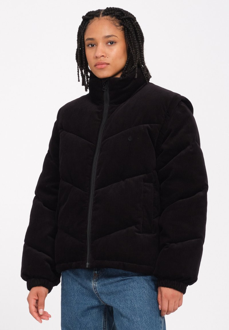 Schwarze Cordjacke mit hohem Kragen, Reißverschluss und gestepptem Design. Verfügt über elastische Bündchen und seitliche Taschen für zusätzlichen Komfort.