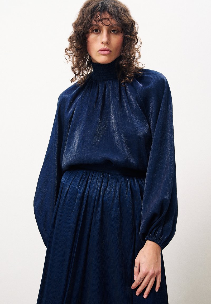 Robe bleu marine à manches longues avec un col montant, un design plissé et un tissu texturé. Présente des manches ballons volumineuses et une taille élastique.