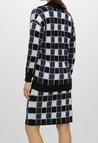 Stickad tröja och kjolset med ett rutigt mönster i marinblått, svart och vitt. Ribbad ärm och nederkant; mjuk textur med en figursydd design.