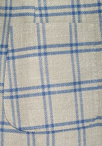 Beige fabric with a textured surface featuring a blue and cream plaid pattern. Visible pocket with rounded edges on the side.