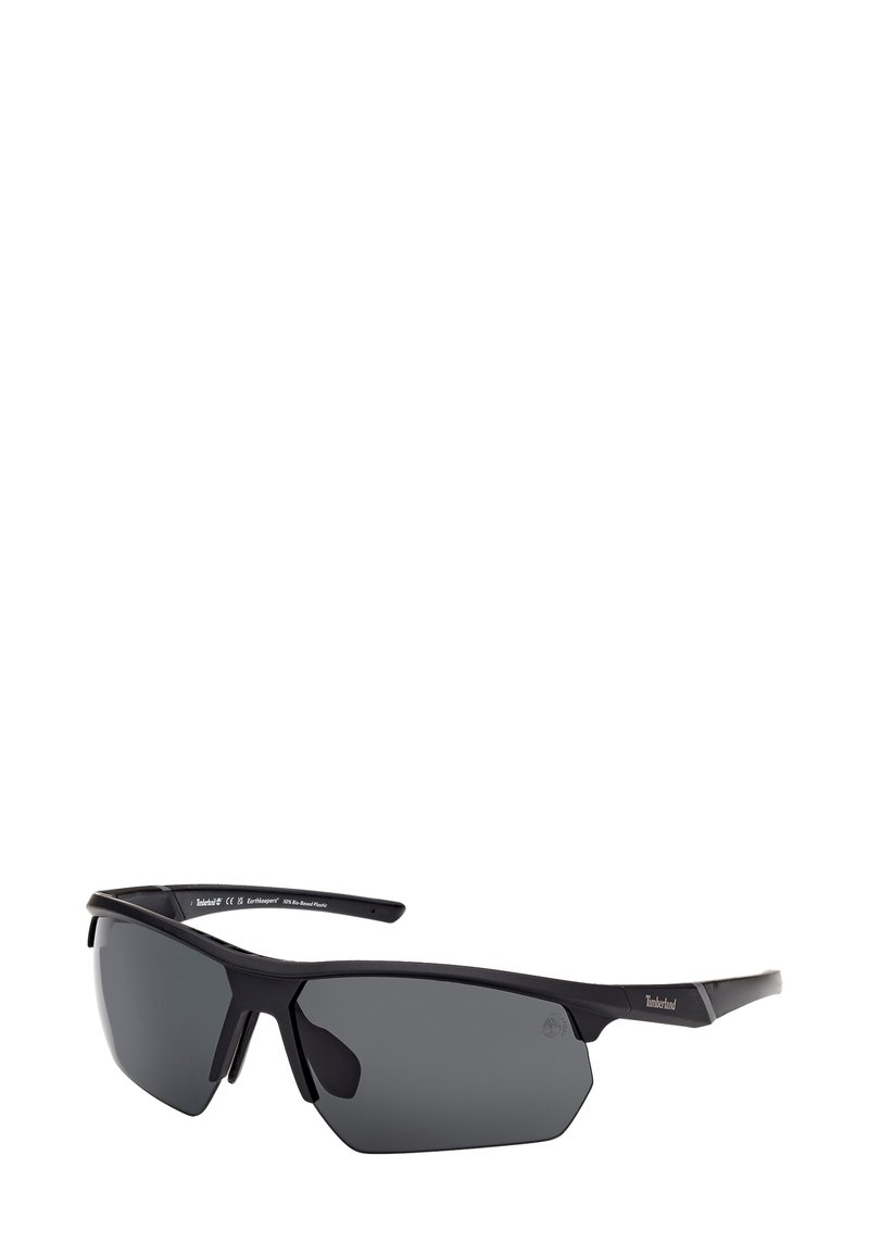 Occhiali da sole con montatura in plastica nera opaca, lenti grigie oscurate, design angolare e dettagli sulle astine. Adatti per l'uso all'aperto.