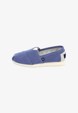 Zapato casual sin cordones con parte superior de tela azul, suela blanca y pequeñas etiquetas de tela en el lateral y el talón, mostrado desde una vista lateral.