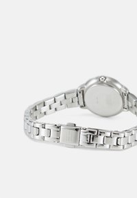 Closed silver metal link watch bracelet with a clasp featuring an engraved rectangular logo, shown with the watch face turned down.
