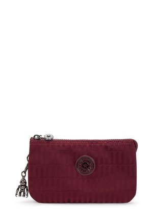 Burgundy zippered pouch with a textured finish, featuring a circular emblem and a small charm. Compact size with a sleek design.