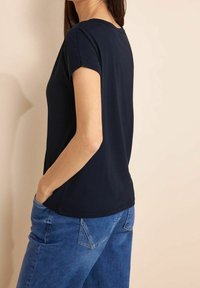 Námořnická modrá krátkosrstá tričko vyrobené z měkké bavlny, s kulatým výstřihem a uvolněným střihem, v kombinaci se světle modrými džíny.
