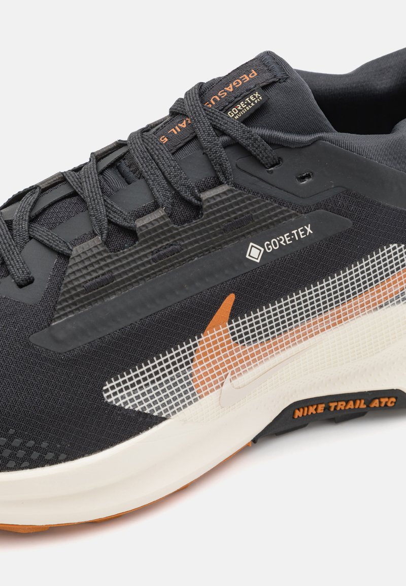 Zapatilla de running GORE-TEX con parte superior de textil negro, acentos en naranja y blanco, panel de malla y suela texturizada y acolchada.