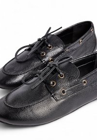 Zapatos de cuero negro con un acabado texturizado, punta redonda, cordones y acentos de hardware dorado en los laterales. Diseñados para un uso casual.