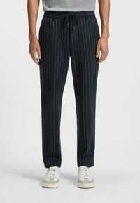 Marinrandiga byxor med dragsko i midjan, som har en avslappnad passform och mjukt tyg. Kombinerat med ljusa sneakers på en neutral bakgrund.