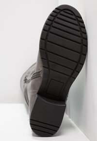 Bottine en cuir gris avec surface texturée, semelle en caoutchouc et motif de bande de roulement rainuré. Détail de fermeture éclair latérale visible sur la tige.