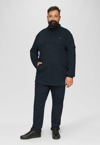 Haut à capuche marine avec un col montant, un cordon de serrage et une poche avant. Associé à un pantalon marin et des baskets noires. Tissu lisse et coupe décontractée.