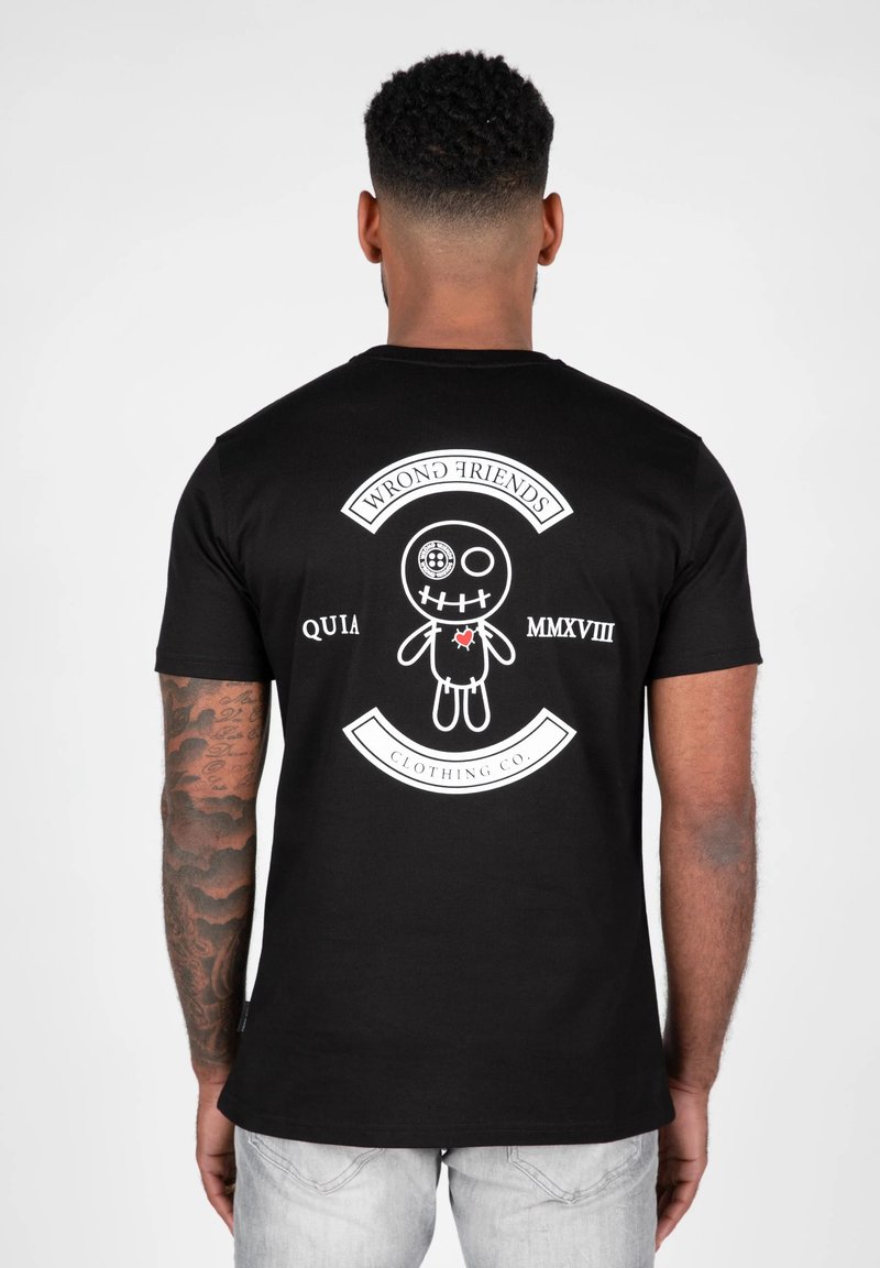 Sort bomulds t-shirt med et hvidt grafisk print på ryggen, der inkluderer en karikaturdukke, tekst og dekorative elementer. Kortærmet og med rund hals.