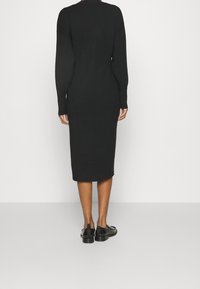 Robe midi noire en maille avec manches longues, silhouette ajustée et texture côtelée. Associée à des chaussures noires au design élégant.