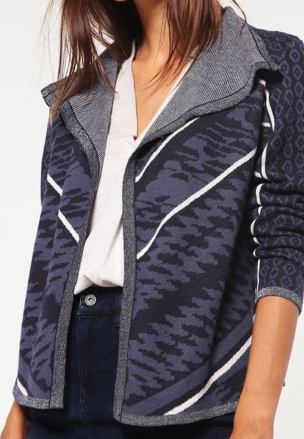 Stickad jacka med grå och marinblå mönstrad design, utrustad med en bred krage och vita accentlinjer. Mjuk struktur och öppen frontstil.