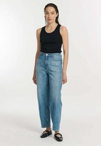 Czarny bezrękawnik zestawiony z wysokimi spodniami dżinsowymi w jasnoniebieskim kolorze. Gładka faktura, prosty krój nogawek oraz subtelne detale w przeszyciach.