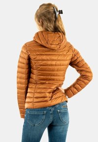 Veste marron matelassée et gonflée avec un motif matelassé horizontal, capuche et manches longues, associée à un jean bleu. Texture lisse.