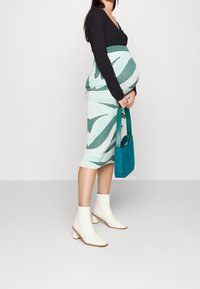 Zelená a bílá vzorovaná pletená sukně, černý top s dlouhými rukávy, bílé kotníkové boty, držící tyrkysovou kabelku. Hedvábná, těsně padnoucí silueta.