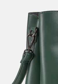 Dunkelgrüne Ledertasche Nahaufnahme mit einem abnehmbaren Riemen mit silbernem Metall-Drehverschluss und genähten Details.
