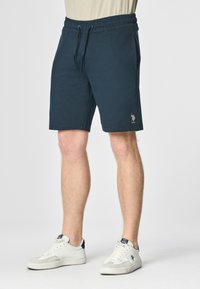 Shorts in cotone blu navy con vita elastica, cordoncino e tasche laterali. Presentano un piccolo logo ricamato sulla parte bassa della gamba sinistra.