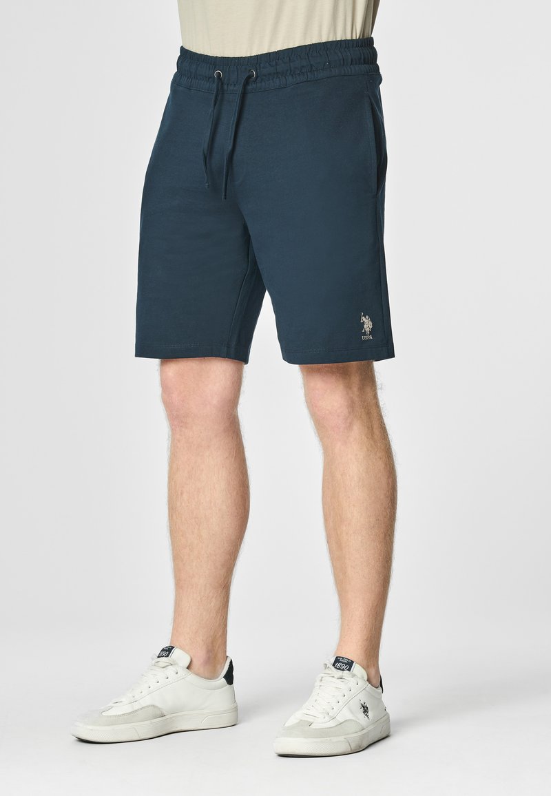 Shorts in cotone blu navy con vita elastica, cordoncino e tasche laterali. Presentano un piccolo logo ricamato sulla parte bassa della gamba sinistra.