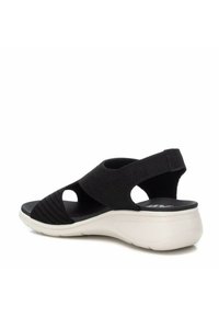Sandalia negra con correas elásticas duales, diseño de punta abierta y suela blanca acolchada. Presenta una parte superior texturizada y soporte seguro para el talón.