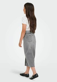 Pilkas džinsinis sijonas su aukštu juosmeniu ir užpakalinėmis kišenėmis, derinamas su balta trumpomis rankovėmis marškiniais, ant kurių yra mažų juodų taškų, dėvimi su juodais batais.