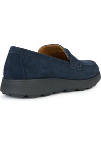 Zapatos náuticos de ante azul marino, tipo slip-on, con punta redondeada y suela baja de goma negra, que presentan un detalle de costuras en los laterales para mayor textura.